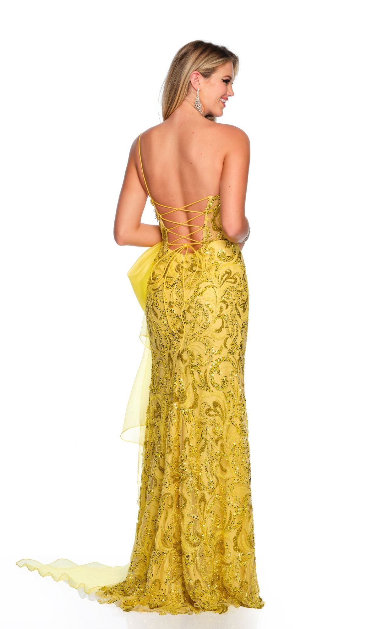 A woman faces away, wearing the Dave and Johnny Long Yellow Prom Dress 11527 with lace-up detailing, sequin embellishments, and a floor-length skirt for an elegant silhouette.